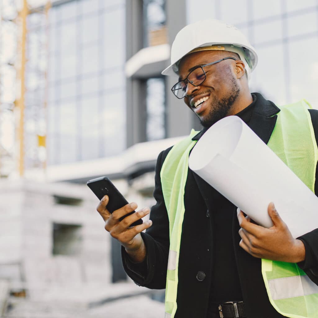 Man engineer standing on construction site, using smartphone